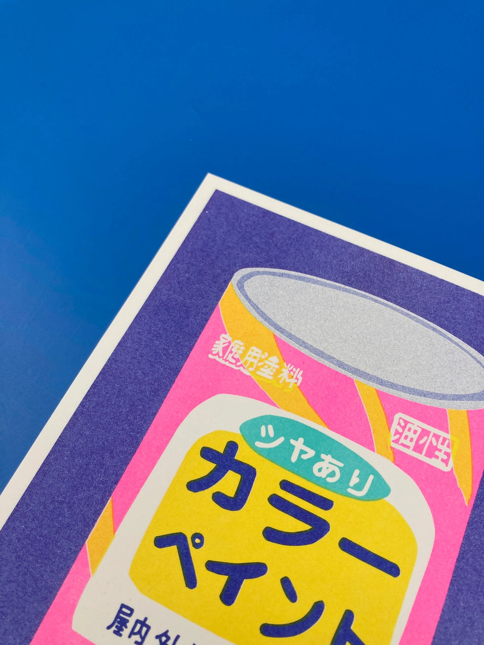 Colorful risograph art print titled Japanese Bucket of Paint by Dutch duo We Are Out Of Office, featuring a retro Japanese paint can in bright fluorescent pink, purple, and yellow tones. Hand-printed with rice-based inks on Biotop 300g paper, perfect for pop art and design lovers.