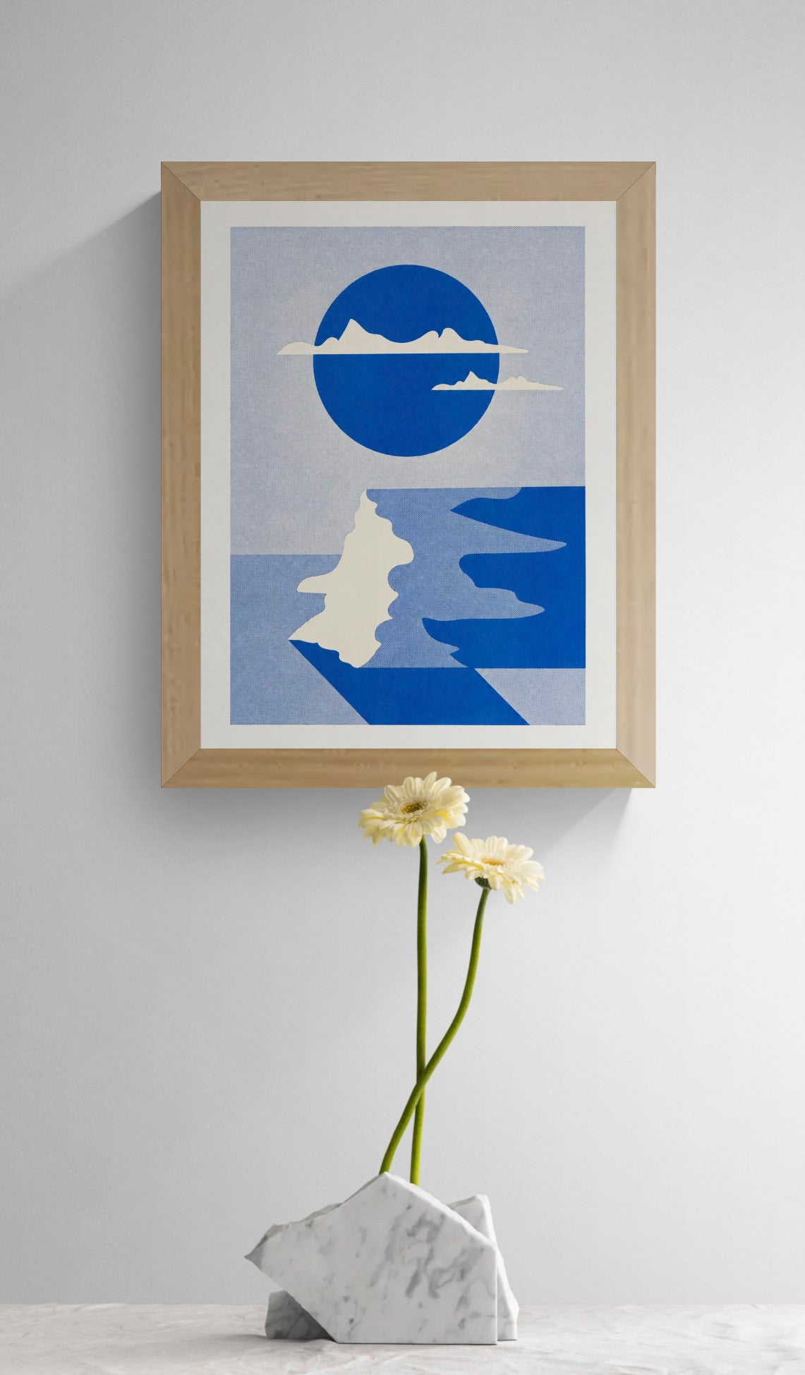Vertical risograph art print by PTRVRKD featuring an abstract coastal cliff landscape, a large cobalt blue circle, cream mountain silhouettes and winding blue water. Minimalist geometric wall art in textured blue tones.