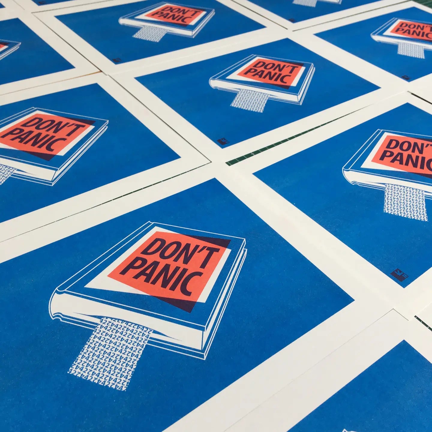 Risograph art print titled Book by VrijFormaat, featuring a blue book cover with bold red and black lettering reading “DON’T PANIC”, inspired by The Hitchhiker’s Guide to the Galaxy. Minimalist design printed in red and blue vegetable-based inks on Biotop paper, A4 size.
