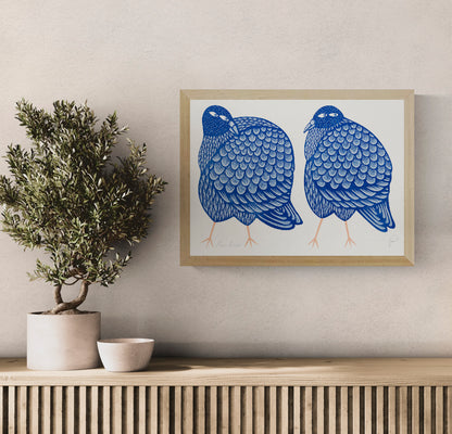 Two plump pigeons illustrated in deep blue and pale blue with peach legs, detailed patterned feathers and playful expressions, horizontal A3 risograph wall art for colourful modern interiors.