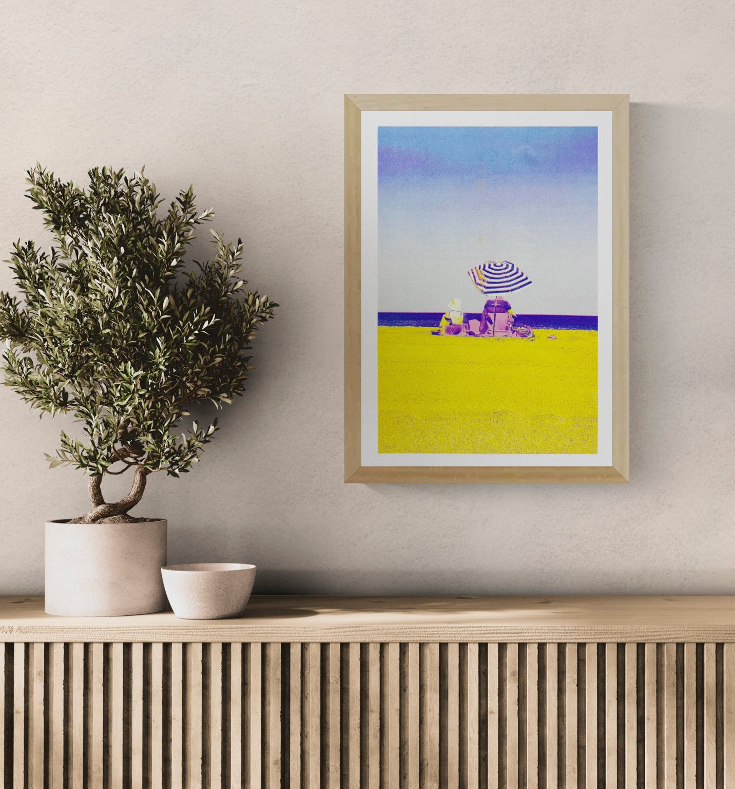 Colorful risograph art print titled “Basque Beach” by PTRVRKD, featuring two people sitting under a striped umbrella on a bright yellow beach with a soft blue-purple sky; A3 limited edition printed on Munken Pure Rough paper. Vibrant modern beach artwork ideal for coastal decor and contemporary wall art collectors.