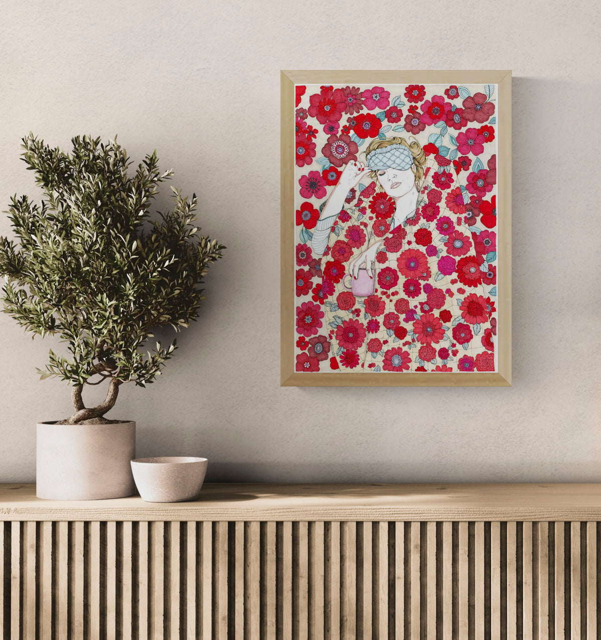 Art print by Ana Jarén showing a woman wrapped in a vibrant floral duvet with a pink coffee mug in hand, surrounded by delicate red and pink flowers — cosy, feminine, and ideal for interior decoration.