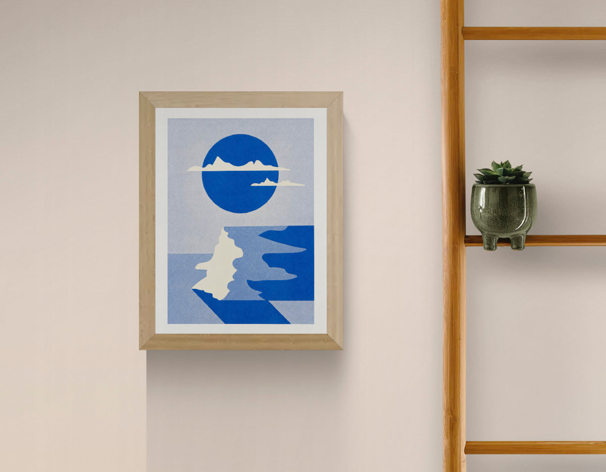 Vertical risograph art print by PTRVRKD featuring an abstract coastal cliff landscape, a large cobalt blue circle, cream mountain silhouettes and winding blue water. Minimalist geometric wall art in textured blue tones.