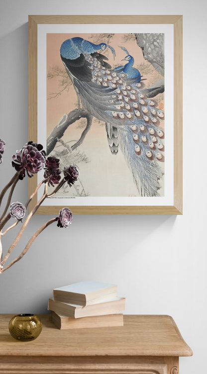Two blue peacocks perched on a pine tree branch in a vintage Japanese woodblock style by Ohara Koson, with peach, grey and cream tones. Vertical digital art print for elegant wall decor.