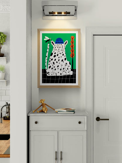 Badass by Dans les Dents, vertical giclée art print of a playful black-spotted white cat wearing a blue beanie, holding a dragonfly against a bright green background with orange plants. Bold, contemporary wall art.