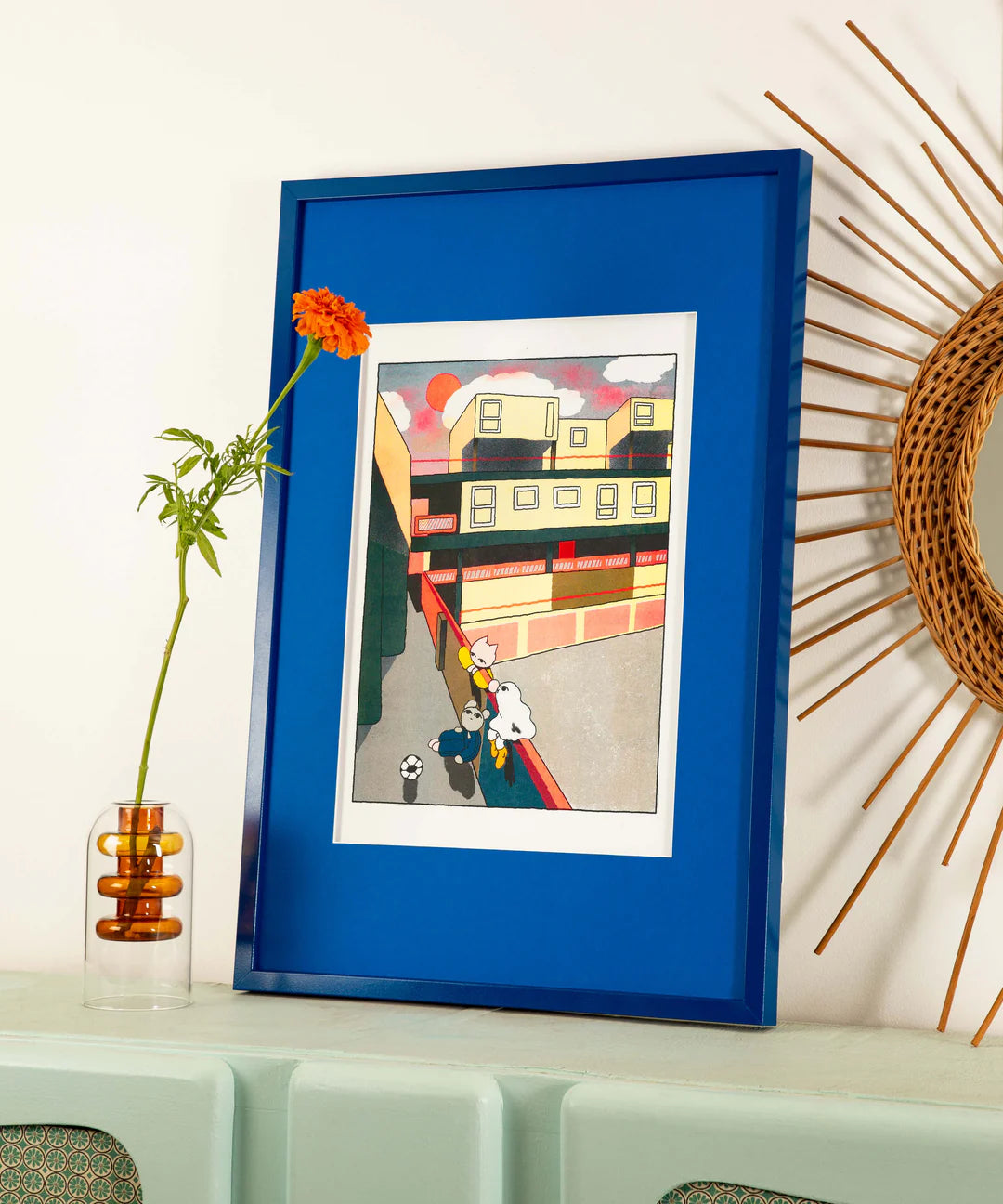 Colorful risograph print Estate Hang by Hel Covell showing three playful characters and a soccer ball in a modern urban courtyard at sunset, with geometric buildings and warm orange light — a nostalgic and tender artwork celebrating friendship and everyday life.