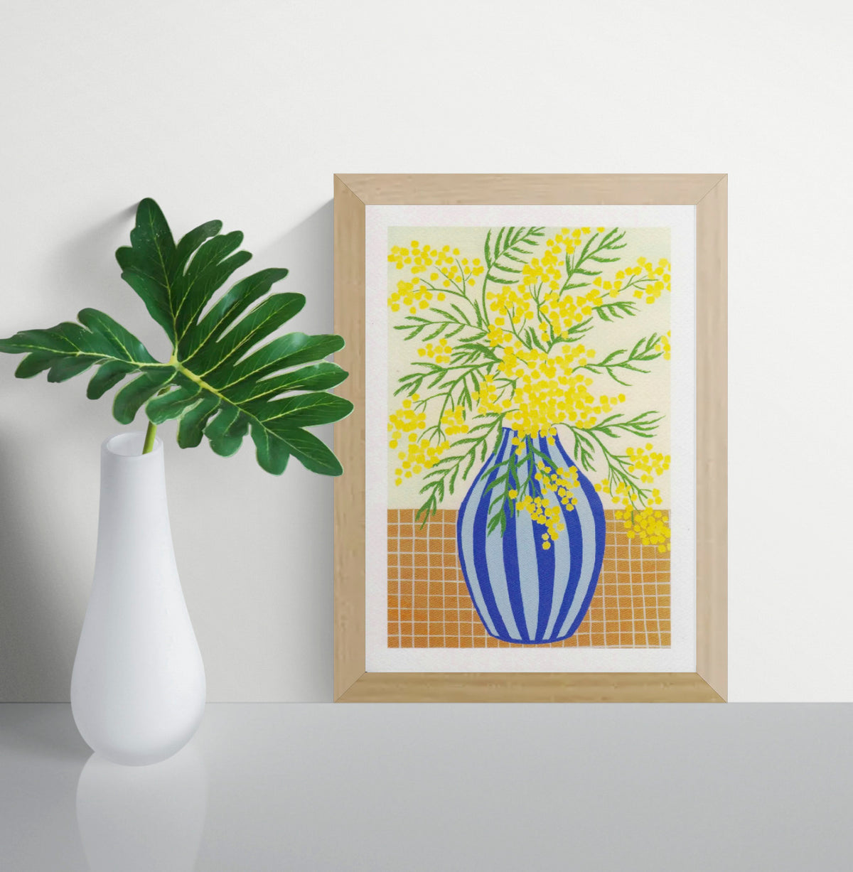 Botanical digital art print titled “Mimosa” by Belgian illustrator Leens, featuring vibrant yellow mimosa flowers in a blue striped vase on a tiled table, printed on textured fine art paper in A4 size.