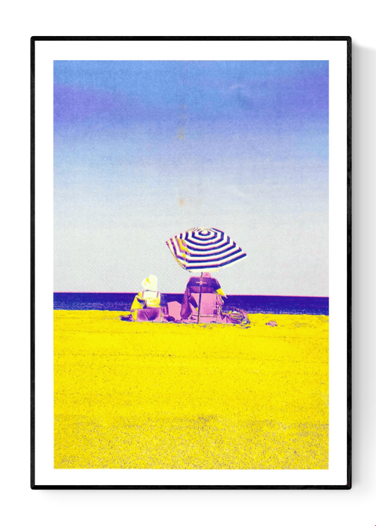Colorful risograph art print titled “Basque Beach” by PTRVRKD, featuring two people sitting under a striped umbrella on a bright yellow beach with a soft blue-purple sky; A3 limited edition printed on Munken Pure Rough paper. Vibrant modern beach artwork ideal for coastal decor and contemporary wall art collectors.
